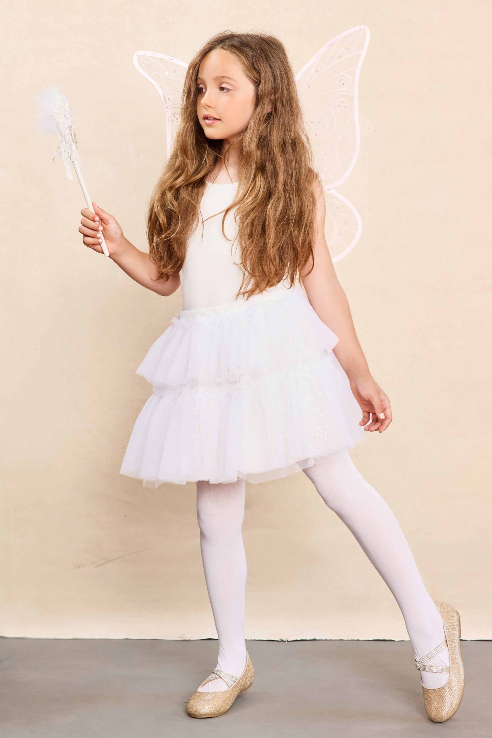 Young girl in a white dress with fairy wings and a wand on a beige background