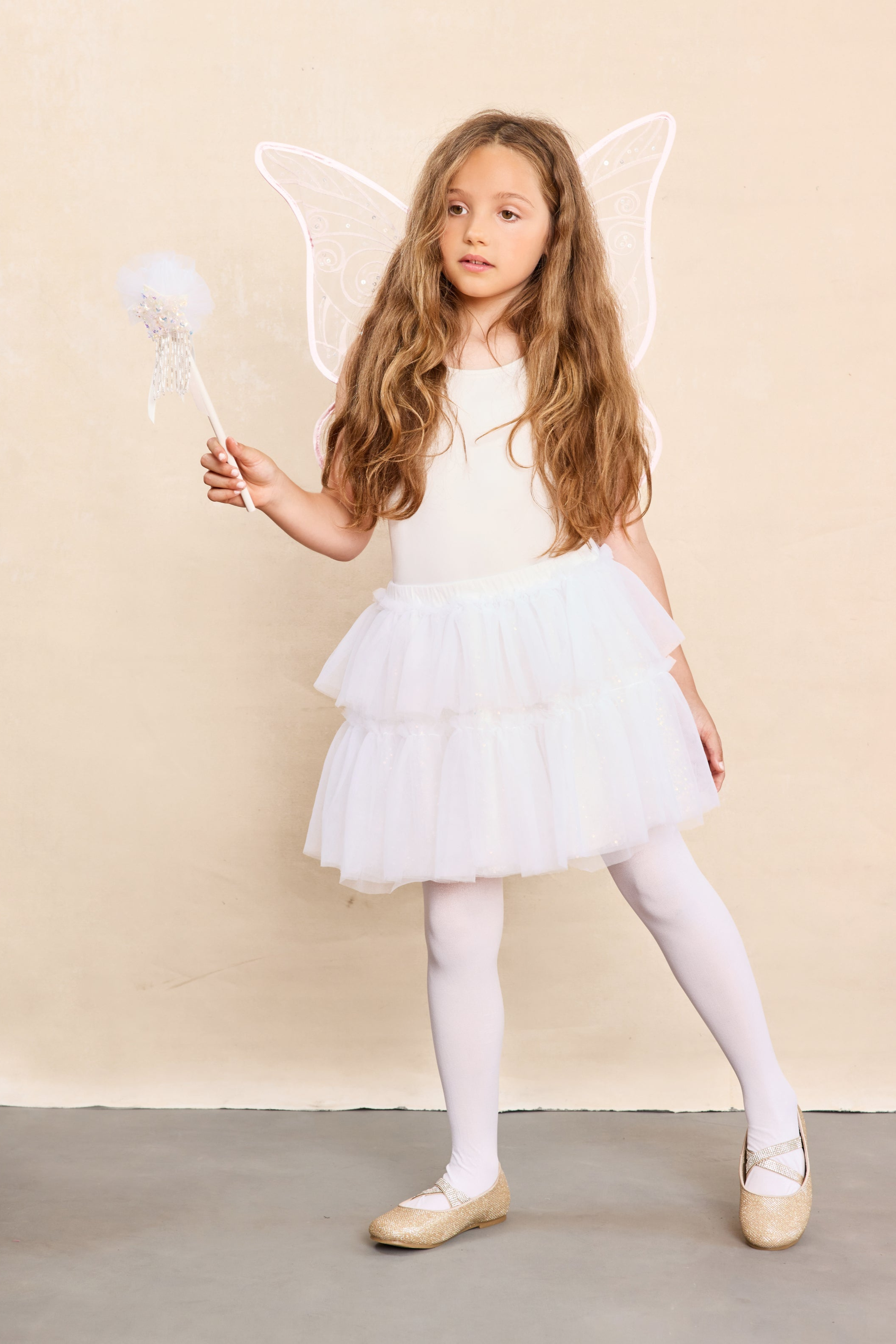 Young girl in a white angel fairy costume with wings and a wand against a beige background