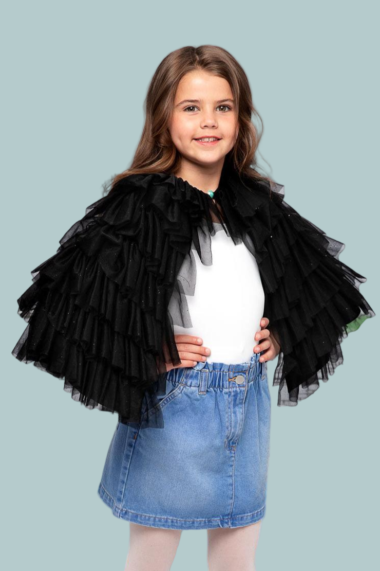 Young girl wearing a black ruffled jacket over a white shirt and blue denim skirt on a light blue background