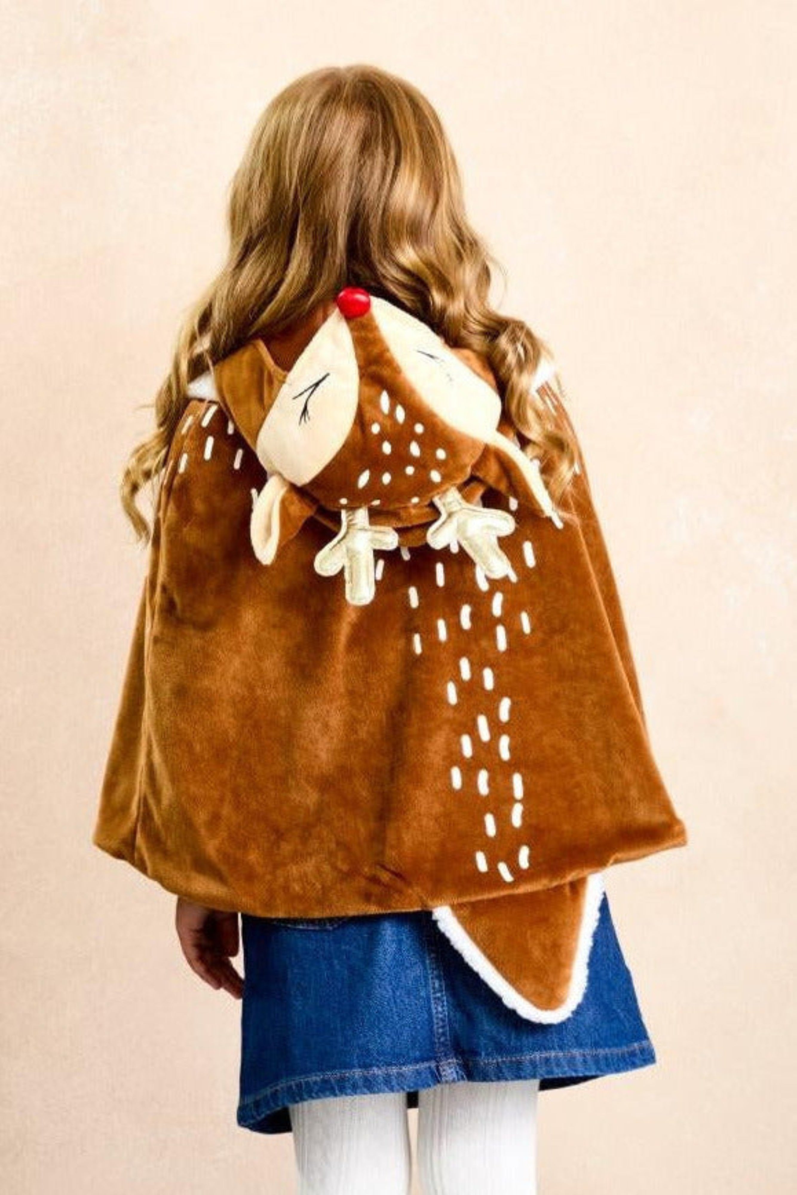Child wearing a reindeer 
themed cape with a red nose and white accents on a beige background